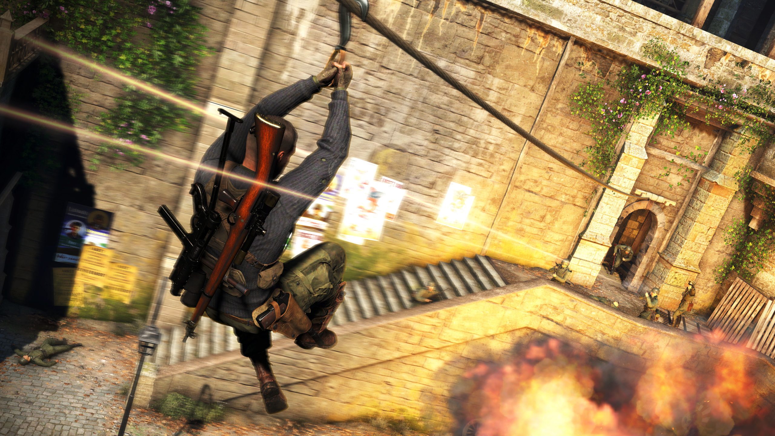 A screenshot from Sniper Elite 5. A man with a buzzcut, wearing a blue shirt and camo pants with two guns strapped to his back, zips down a zipline towards three men in camo pointing guns at him. Two other men appear to be running. Another lies motionless on the ground.